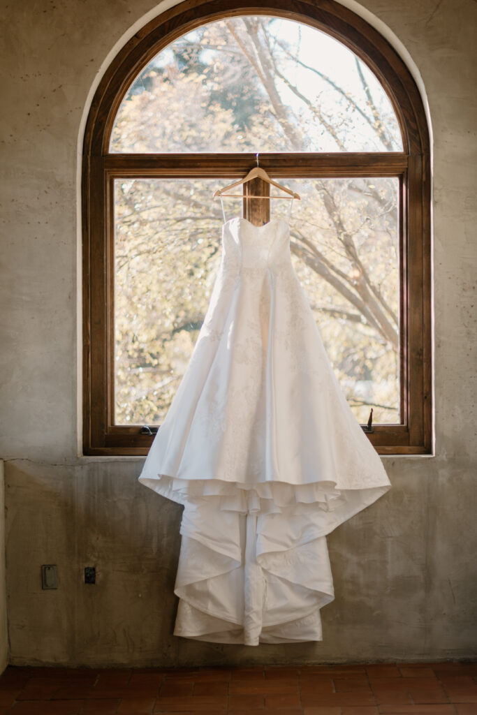strapless, long wedding gown hung up on hanger on window pane 