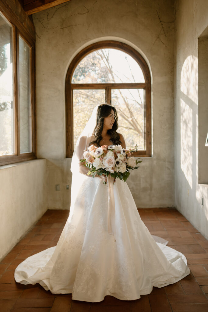 bride holding flower bouquet and standing in hallway with large windows and tons of natural light