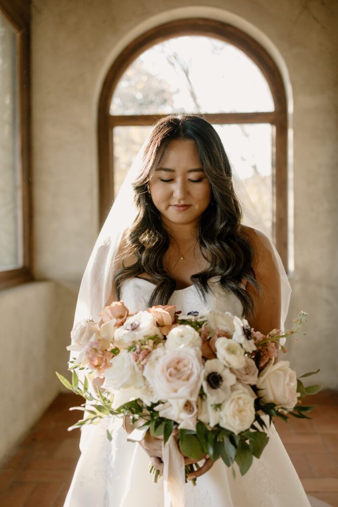 bride holding flower bouquet and standing in hallway with large windows and tons of natural light