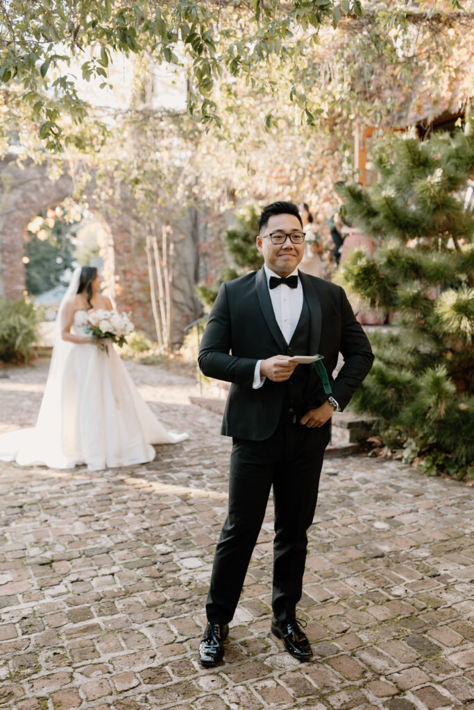 bride and groom first look outside in courtyard with brick wall behind and tons of greenery