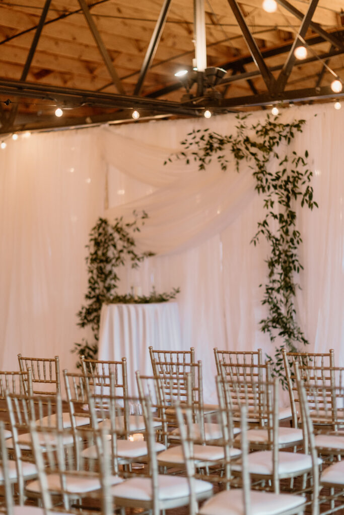modern wedding venue with gold and white chairs in front of simple wedding arch