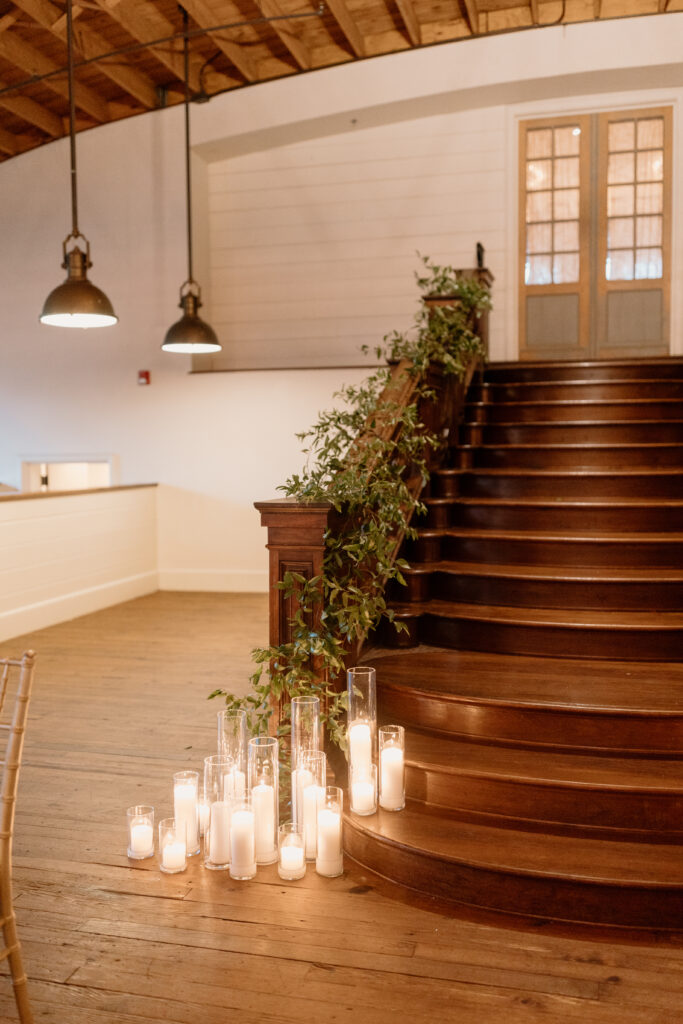 lit candles at bottom of staircase that has greenery around rail of stairs