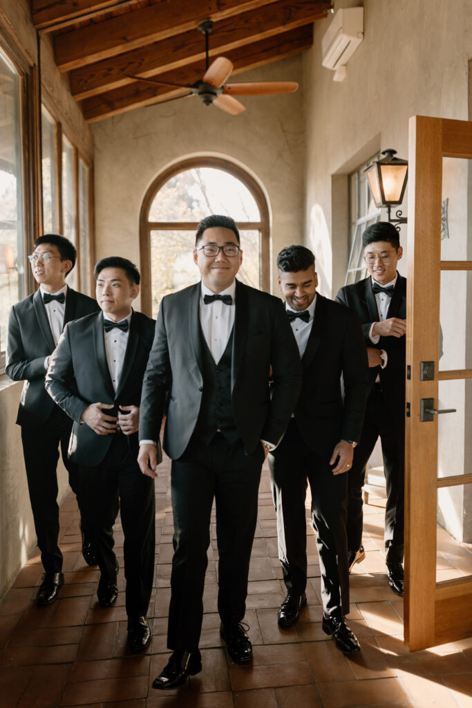 groom and groomsmen walking down hall together after getting dressed for wedding ceremony