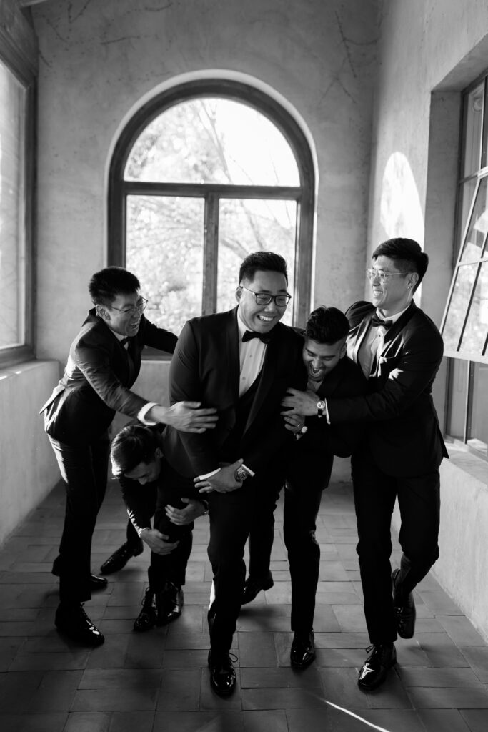 groom and groomsmen standing and laughing at each other while posing in front of window