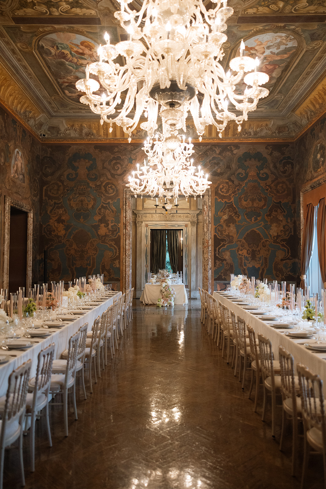 Candlelit reception ballroom at Villa Erba during a Lake Como wedding, long banquet tables beneath Murano glass chandeliers and ornate Baroque painted walls