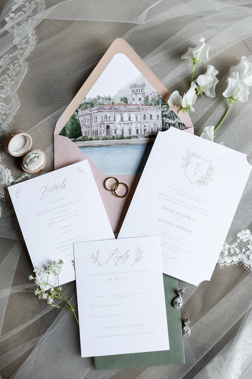 Full Lake Como wedding invitation suite for Diah Eljamal and Jenna Ahmad at Villa Erba, displayed with gold wedding bands, a diamond engagement ring in a velvet box, crystal drop earrings, white sweet pea flowers, and a blush envelope lined with a watercolor illustration of the estate