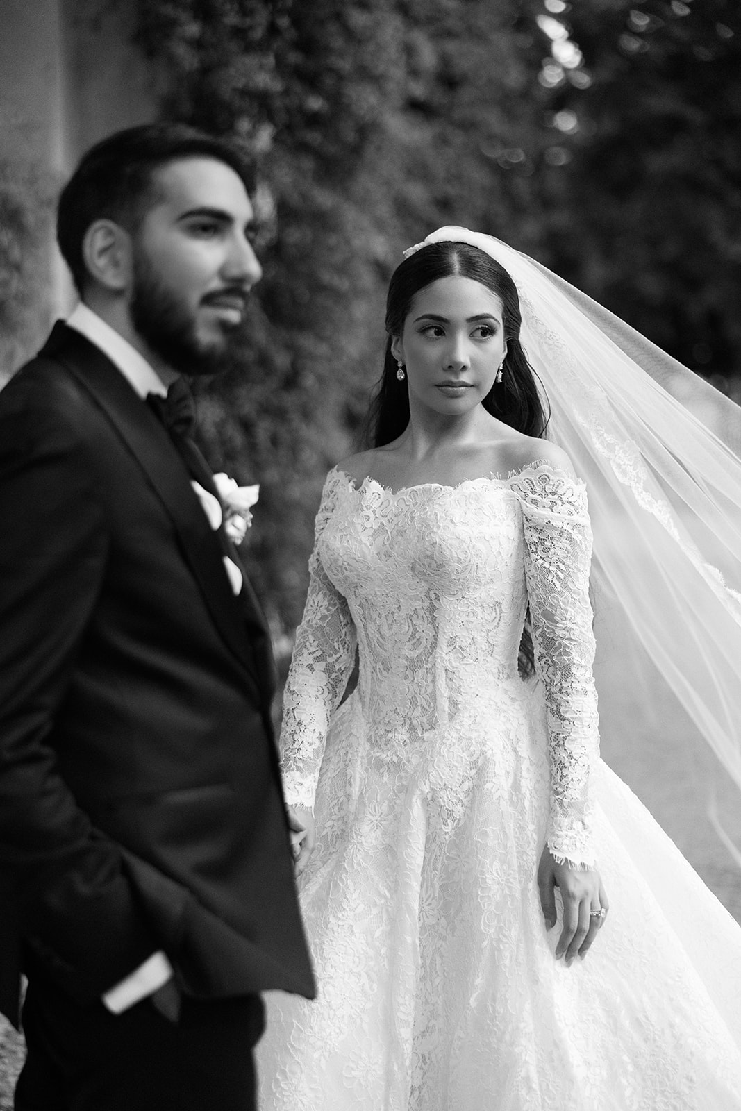 Black and white close-up portrait of bride in off-shoulder lace gown and cathedral veil beside groom in black tuxedo at Villa Erba